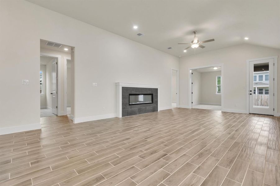 A living space offers a fireplace, wood-look tile flooring, and a ceiling fan, with a glimpse into an adjoining room.