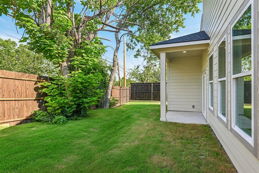 Spacious backyard with a covered concrete patio, wood privacy fencing, mature trees, and a manicured lawn