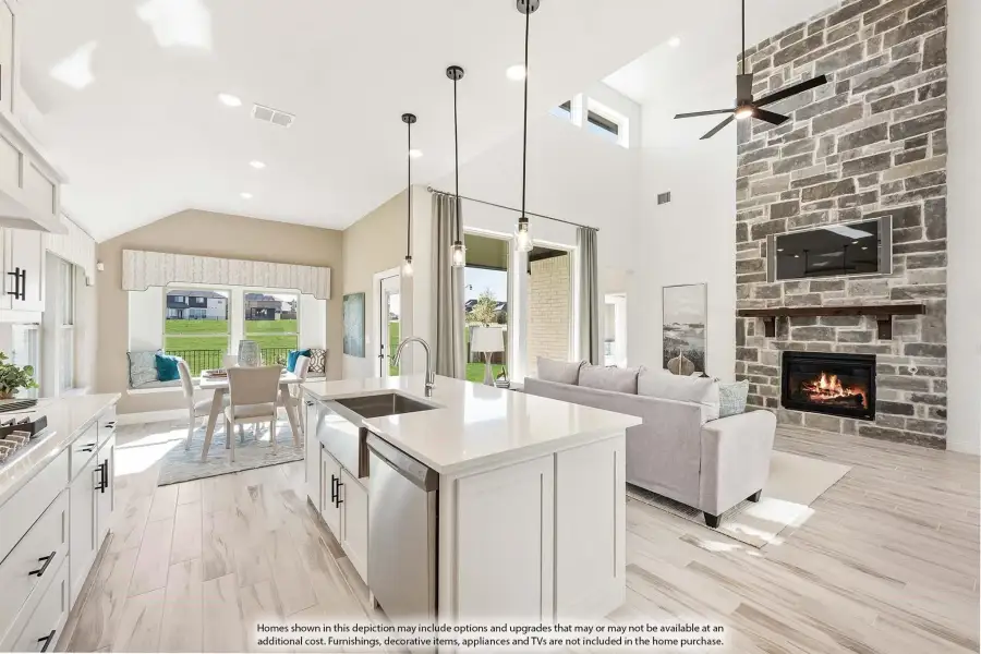 Open-concept kitchen and living area with white island, stone fireplace, vaulted ceiling, and dining space beyond.