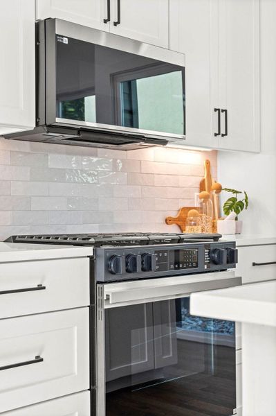 Kitchen with stainless steel appliances, white cabinets, backsplash, and light stone countertops