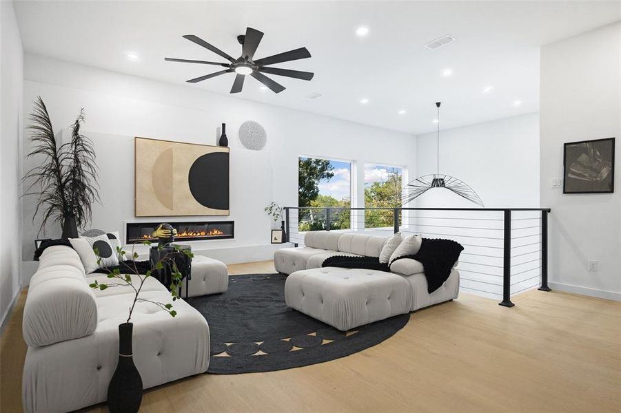 Living room with light wood-style floors, a glass covered fireplace, recessed lighting, and a ceiling fan