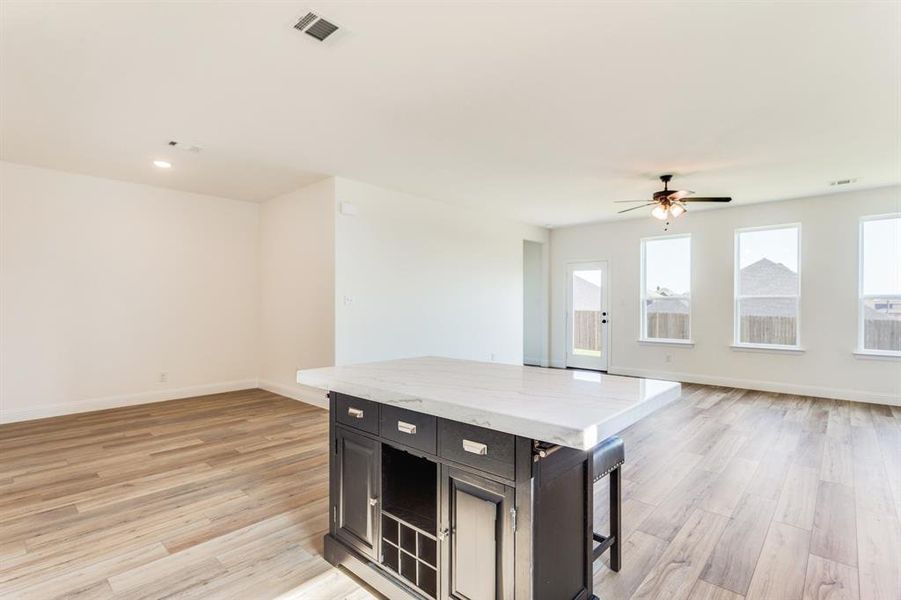 Kitchen with a breakfast bar area, light hardwood / wood-style flooring, a kitchen island, light stone countertops, and ceiling fan