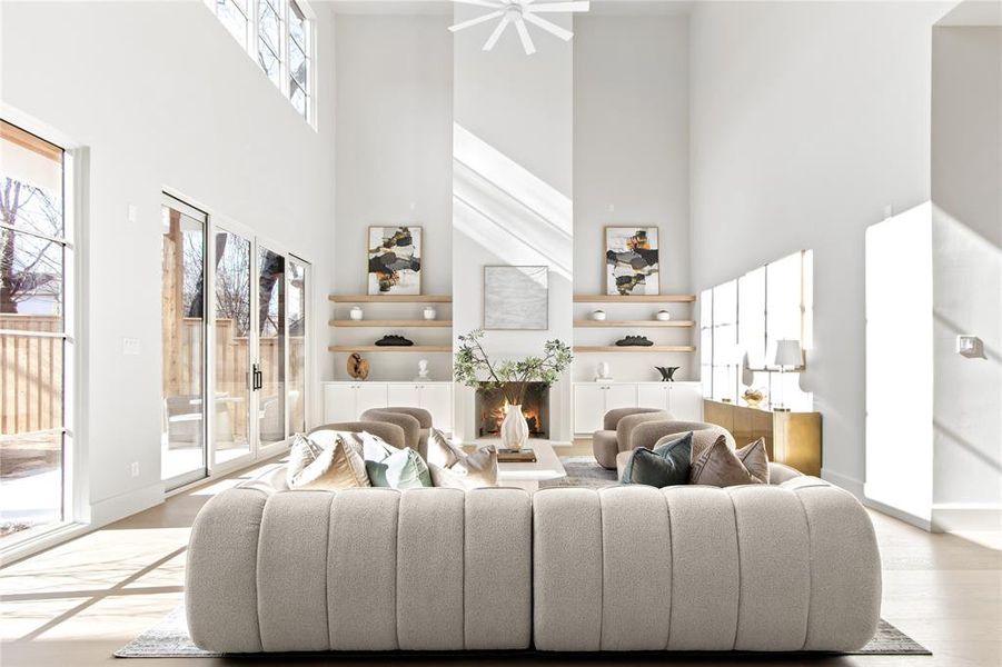 Spacious living area featuring a double-height ceiling, large sliding glass doors, a built-in fireplace, and integrated shelving with lower cabinetry