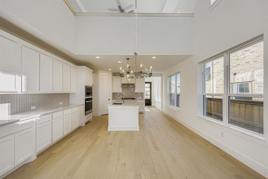 Kitchen with decorative light fixtures, backsplash, light wood finished floors, a kitchen island with sink, and white cabinets