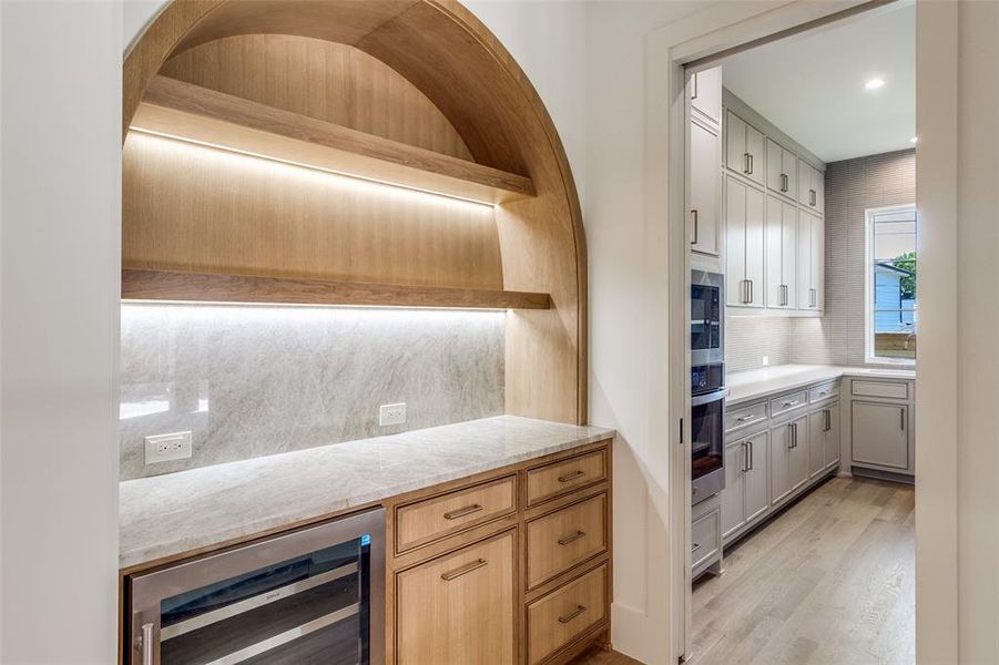 Kitchen featuring wine cooler, backsplash, open shelves, light stone countertops, and light wood finished floors Kitchen featuring wine cooler, backsplash, open shelves, light stone countertops, and light wood finished floors
