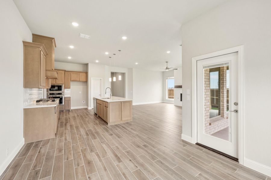 Open-concept kitchen with tan wood cabinets, center island with sink, and light wood-look tile floors opening to living area