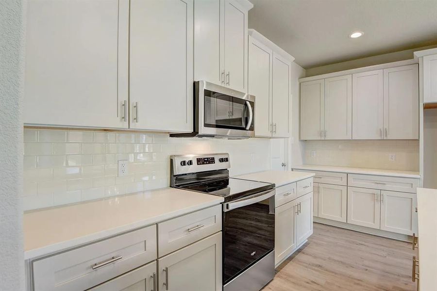 Kitchen featuring stainless steel appliances, decorative backsplash, light countertops, recessed lighting, and white cabinets