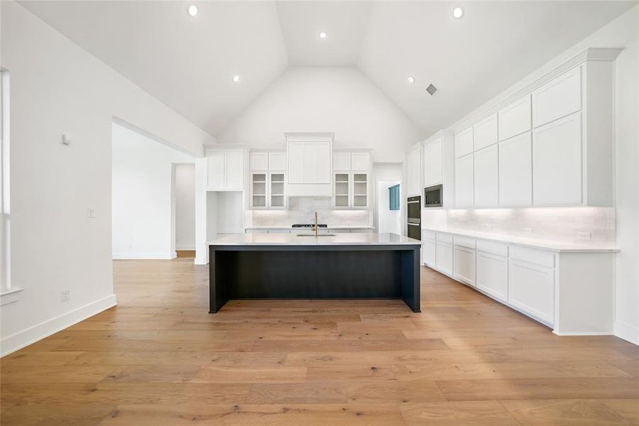 Kitchen featuring white cabinets, decorative backsplash, a kitchen bar, a large island with sink, and high vaulted ceiling
