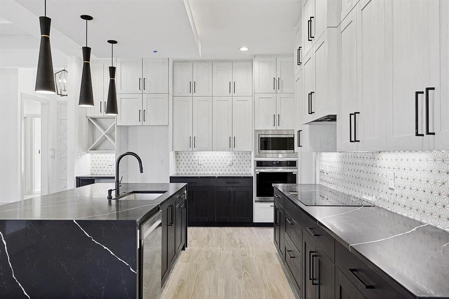 Kitchen with backsplash, stainless steel appliances, a center island with sink, hanging light fixtures, and dark cabinets Kitchen with backsplash, stainless steel appliances, a center island with sink, hanging light fixtures, and dark cabinets