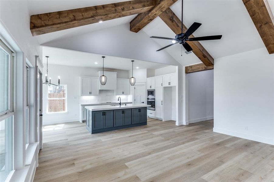 Kitchen featuring beamed ceiling, stainless steel appliances, light wood-type flooring, white cabinetry, and a sink