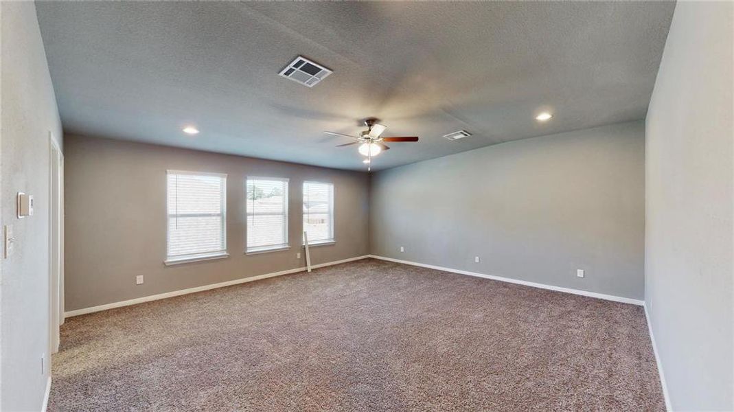 This expansive game room offers a perfect retreat for entertainment and relaxation. With ample space for various activities, it's an ideal spot for family fun or hosting friends. The room is well-lit with multiple windows and features a ceiling fan for added comfort. The neutral palette and plush carpeting provide a versatile backdrop for any decor style. This is a picture of an Elise Floor Plan with another Saratoga Homes.