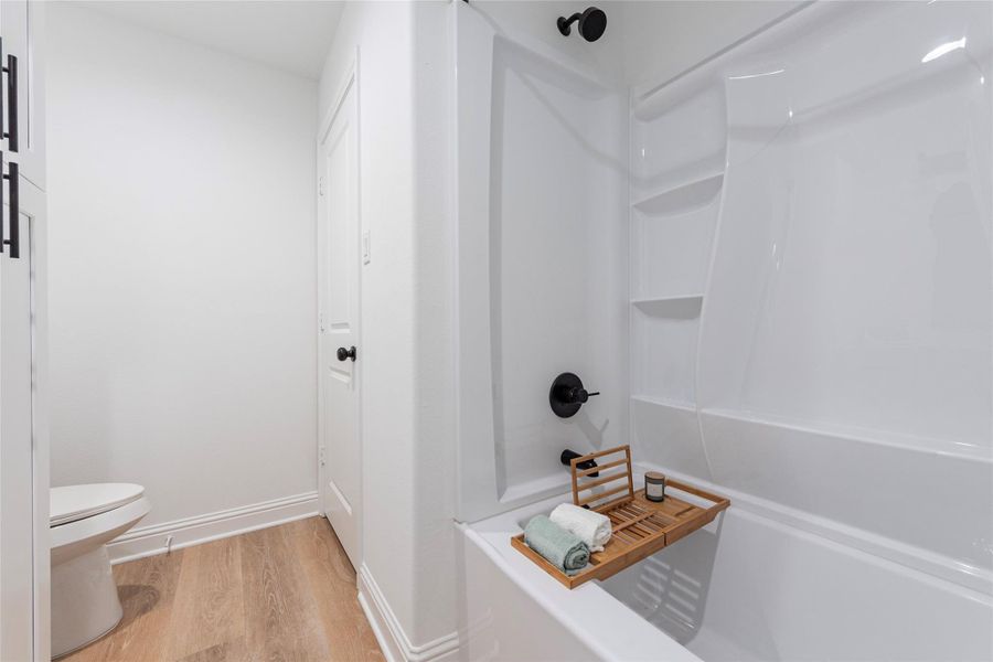 Primary bathroom with linen storage, shower/tub combination and vinyl flooring.