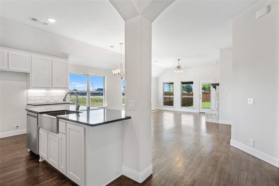 Kitchen with white cabinets, dark wood-style floors, hanging light fixtures, open floor plan, and vaulted ceiling Kitchen with white cabinets, dark wood-style floors, hanging light fixtures, open floor plan, and vaulted ceiling