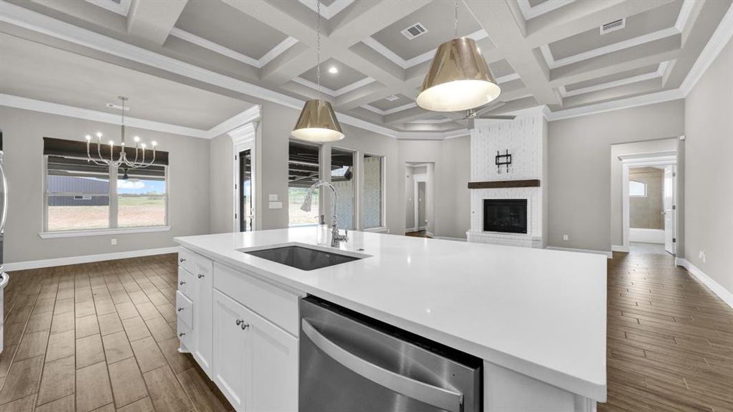 Kitchen featuring coffered ceiling, dishwasher, a kitchen island with sink,  and a brick fireplace