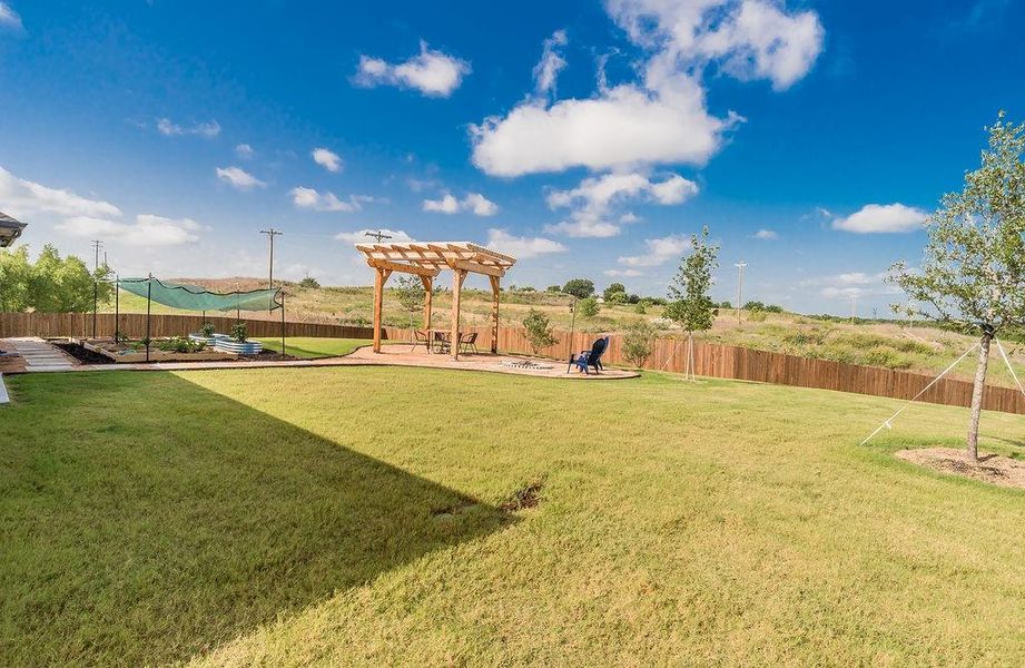 Expansive backyard featuring a large grassy area, a wooden pergola over a patio, and a privacy fence