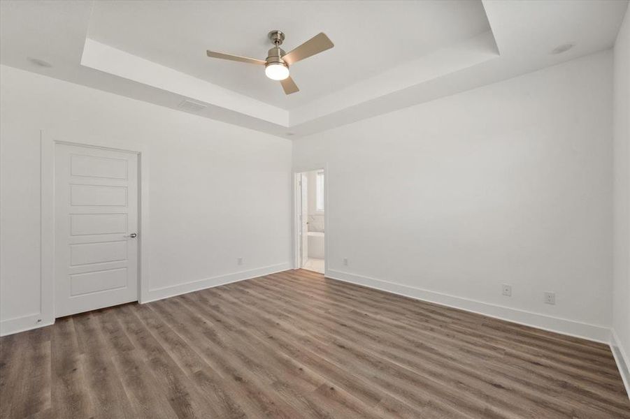 Primary Bedroom with a raised ceiling, LVP finished floors, ceiling fan/light, large walk-in closet, natural lighting  and Ensuite bathroom.