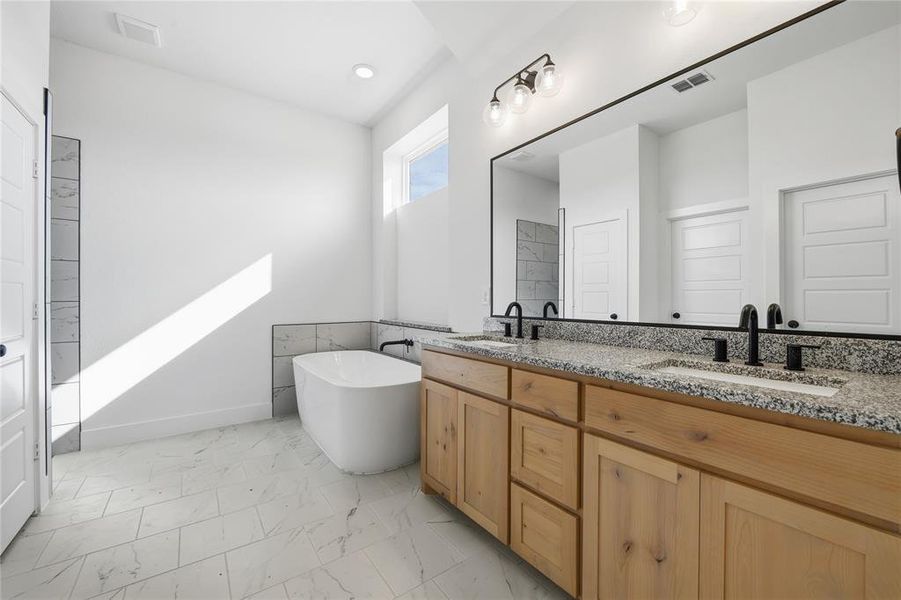 Full bath featuring double vanity, a freestanding tub, and light marble finish flooring Full bath featuring double vanity, a freestanding tub, and light marble finish flooring