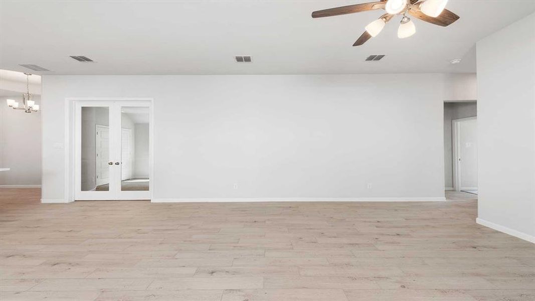 Empty room with ceiling fan with notable chandelier and light hardwood / wood-style flooring