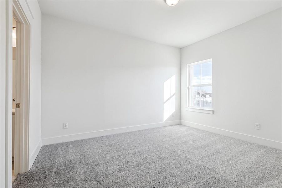 This room features soft grey carpeting, a window providing natural light, and a clean, neutral color palette throughout