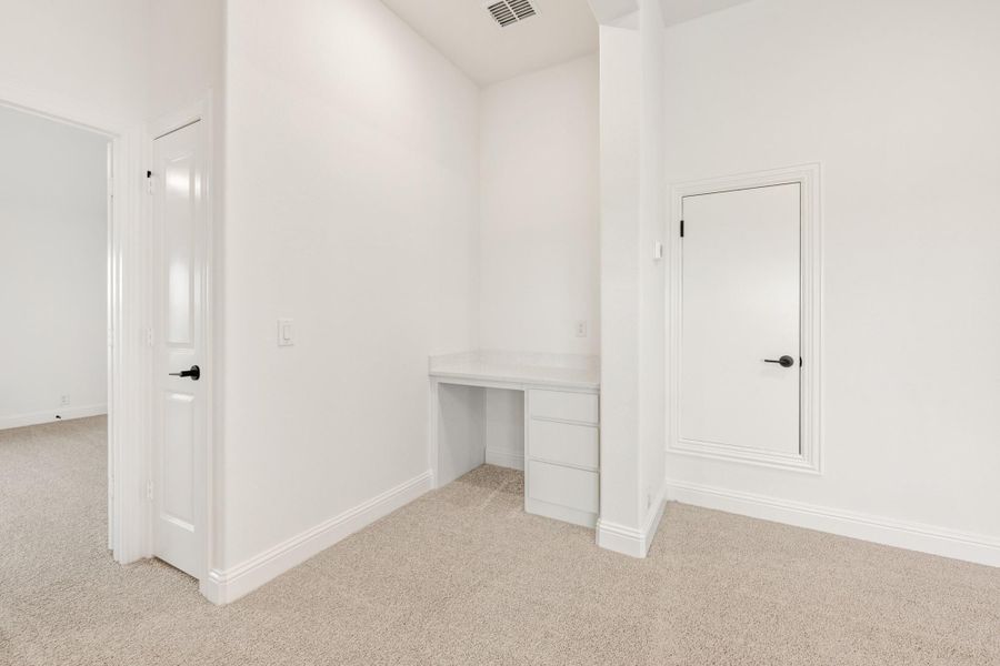 Empty bedroom with built-in white desk, carpet flooring, and two white doors with black hardware
