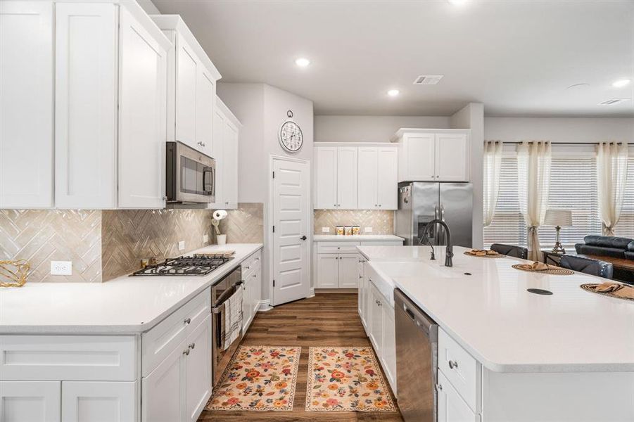 Modern kitchen featuring white shaker cabinetry, stainless steel appliances, white countertops, and wood-finish flooring Modern kitchen featuring white shaker cabinetry, stainless steel appliances, white countertops, and wood-finish flooring