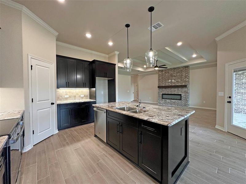 Kitchen with tasteful backsplash, light stone counters, wood tiled floors, hanging light fixtures, and crown molding