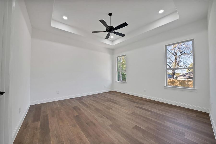Master bedroom with a tray ceiling, dark wood-type flooring, recessed lighting, and a ceiling fan