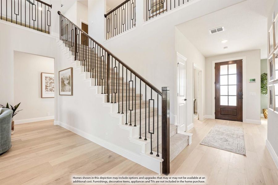 Two-story entryway with staircase, dark iron railings, light hardwood floors, and wood front door with glass panels
