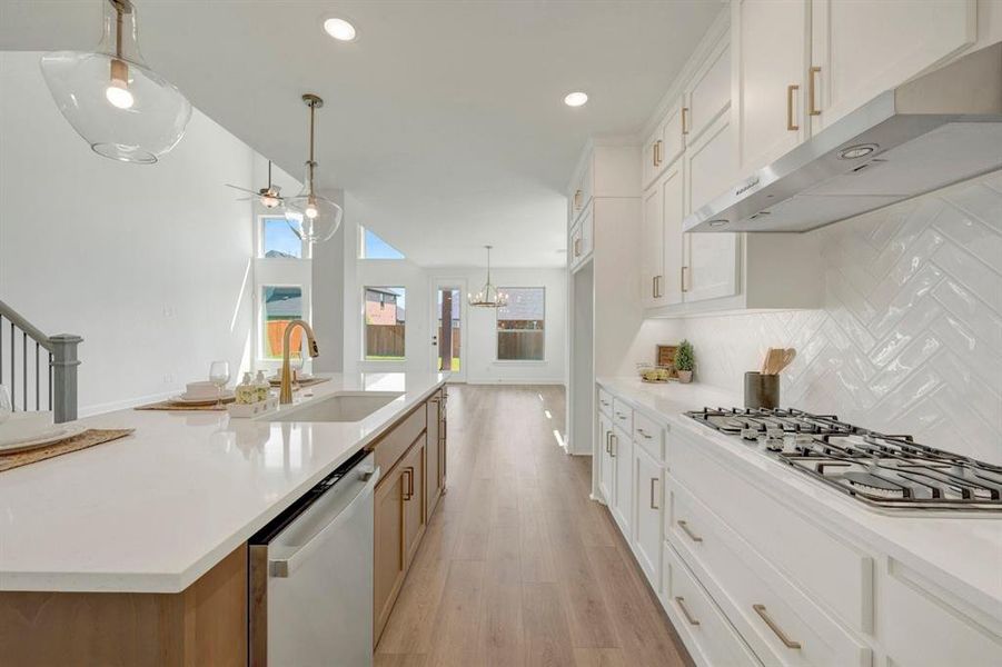 Open-concept kitchen featuring white cabinetry, a gas cooktop, herringbone tile backsplash, and an expansive island with a built-in sink and dishwasher
