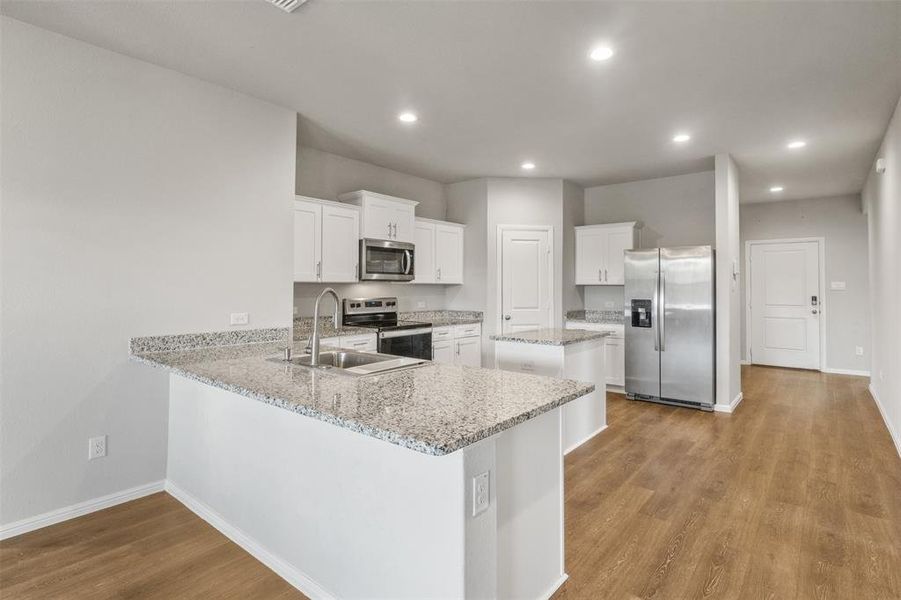 Kitchen featuring appliances with stainless steel finishes, sink, white cabinets, and light hardwood / wood-style floors