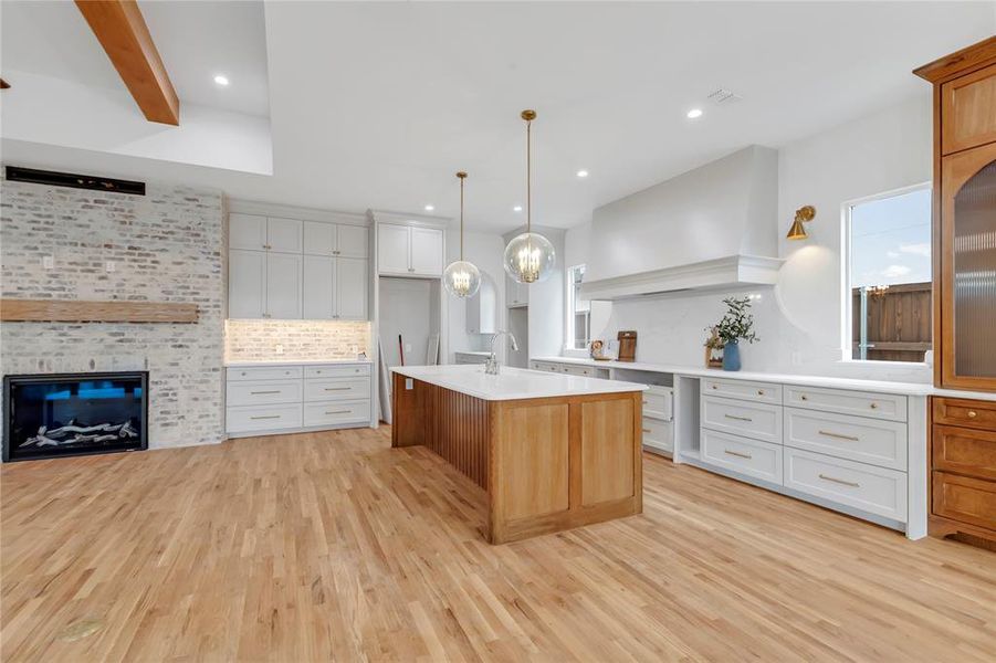 Dual tone kitchen featuring dual tone cabinetry, a kitchen island with sink, open floor plan, a tiled fireplace, and light wood finished floors