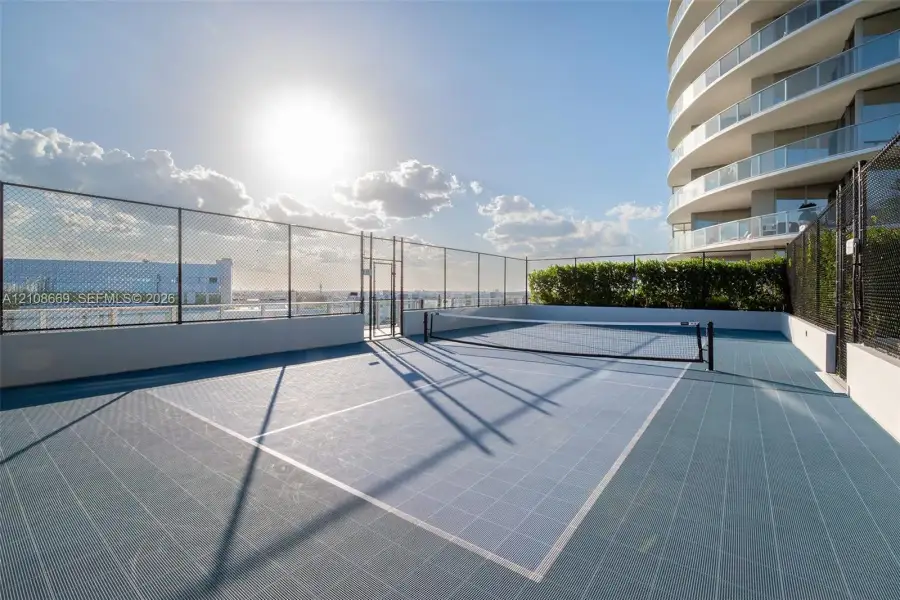 Rooftop sport court featuring blue modular surface tiles, perimeter chain-link fencing, and white masonry walls