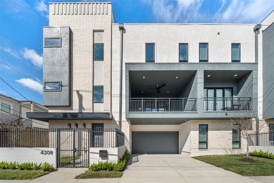 This modern, three-story home features a sleek design with a mix of brick and stucco exteriors. It includes a spacious balcony, large windows for natural light, and a gated entrance. The property also offers a two-car garage and a neatly landscaped front yard.
