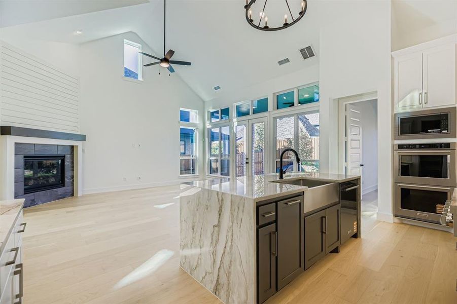 Kitchen featuring high vaulted ceiling, open floor plan, light wood-style floors, appliances with stainless steel finishes, and light stone counters