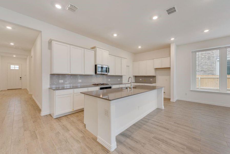 Kitchen with white cabinetry, tasteful backsplash, light hardwood / wood-style flooring, and a kitchen island with sink