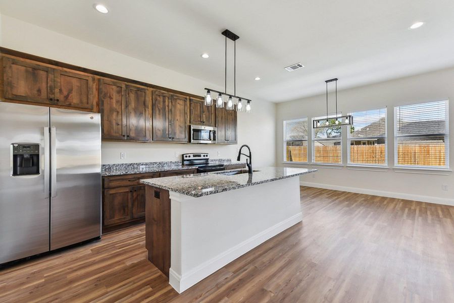Kitchen with wood finished floors, visible vents, stone counters, recessed lighting, and stainless steel appliances Kitchen with wood finished floors, visible vents, stone counters, recessed lighting, and stainless steel appliances