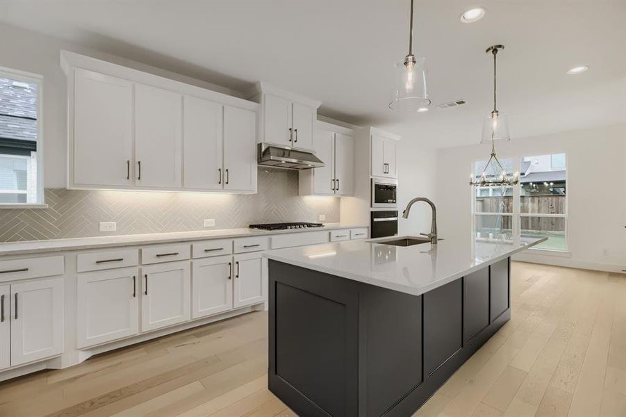 Kitchen with a kitchen island with sink, dual tone cabinetry, light wood-style flooring, hanging lights, and decorative backsplash