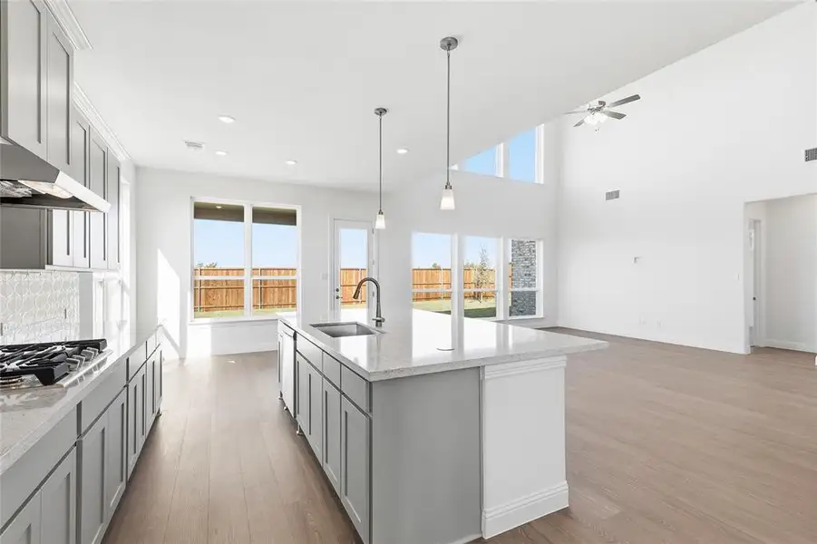 Kitchen with gray cabinetry, light wood-style floors, light stone counters, open floor plan, and a kitchen island with sink Kitchen with gray cabinetry, light wood-style floors, light stone counters, open floor plan, and a kitchen island with sink