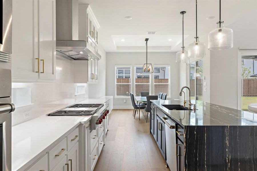 Kitchen featuring a raised ceiling, plenty of natural light, wall chimney range hood, light wood finished floors, and recessed lighting