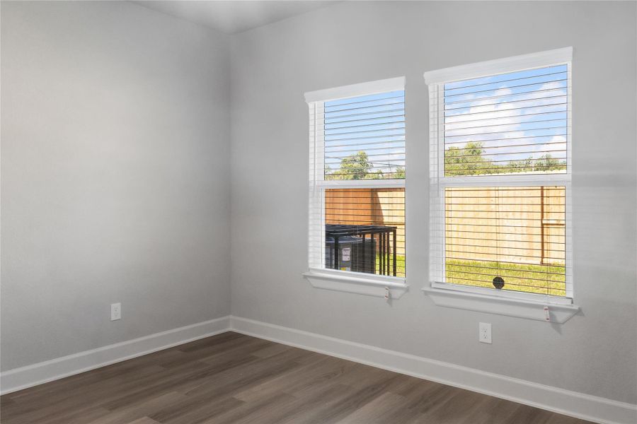 Bright room with two large windows, featuring light gray walls and wood-look flooring, offering a view of a fenced backyard.