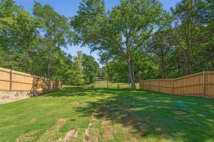 Expansive backyard featuring a manicured lawn, full wood privacy fencing, a stone retaining wall, and mature trees