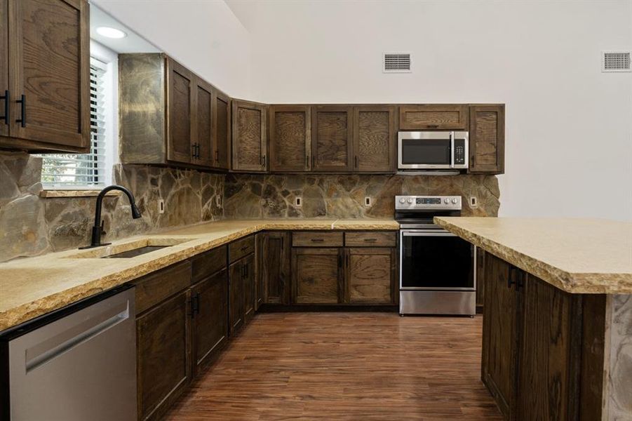 Kitchen featuring dark brown cabinets, appliances with stainless steel finishes, and dark hardwood / wood-style floors