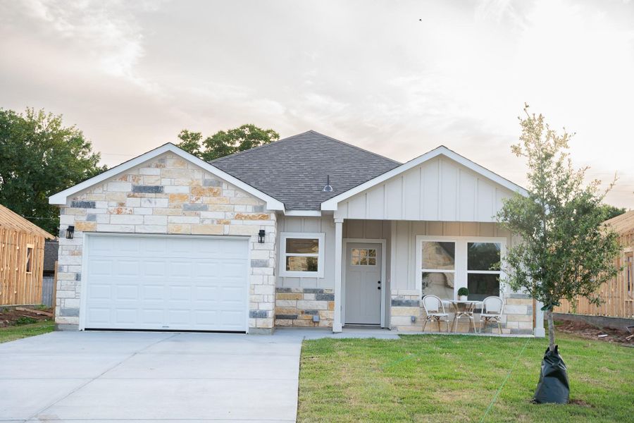 View of front facade with roof with shingles, concrete driveway, stone siding, a garage, and a front yard