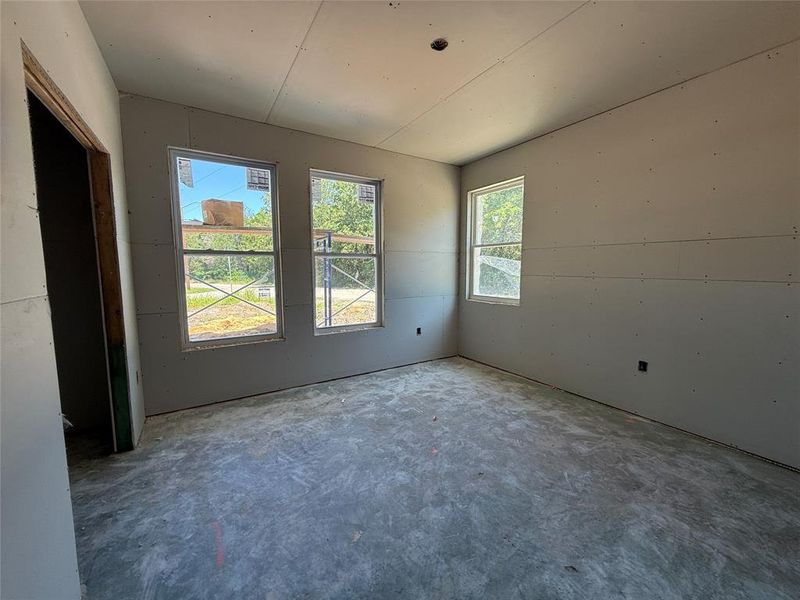Interior room featuring three windows, unfinished drywall, a concrete slab floor, and a doorway