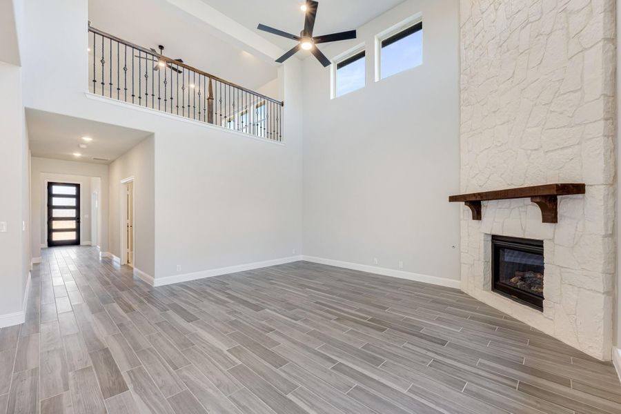 Open living room with two-story ceiling, white stone fireplace, wood mantel, and gray tile floors Open living room with two-story ceiling, white stone fireplace, wood mantel, and gray tile floors