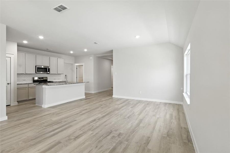 Kitchen with open floor plan, recessed lighting, appliances with stainless steel finishes, light wood-style flooring, and an island with sink