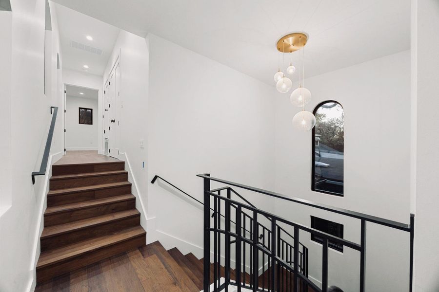 Modern staircase featuring wood-finish treads, black metal railings, and a contemporary multi-orb chandelier