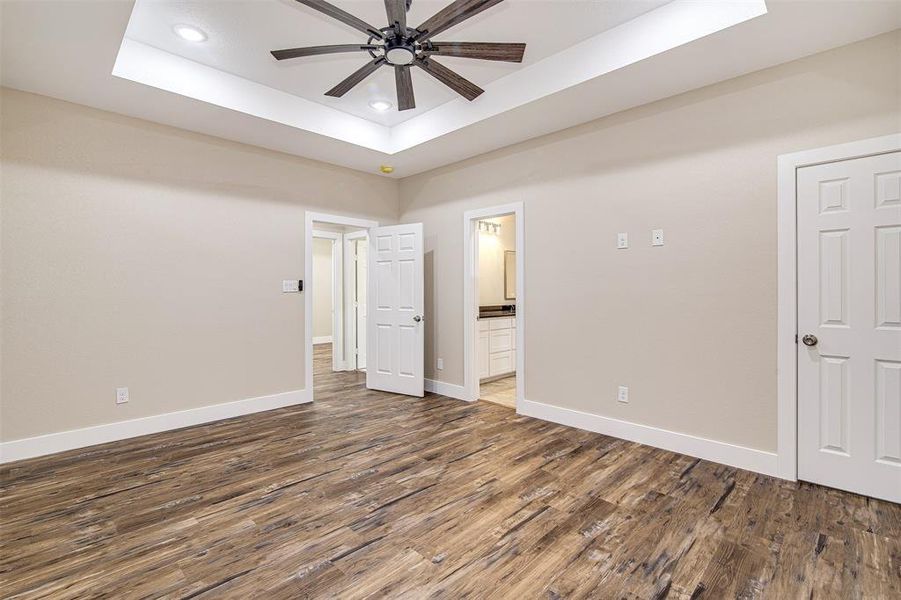 Unfurnished bedroom featuring a tray ceiling, connected bathroom, ceiling fan, and dark hardwood / wood-style flooring