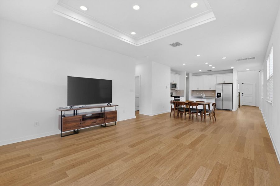 Living room with recessed lighting, light wood finished floors, a tray ceiling, and crown molding