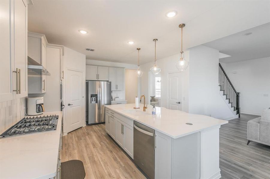 Kitchen featuring sink, an island with sink, decorative light fixtures, decorative backsplash, and appliances with stainless steel finishes